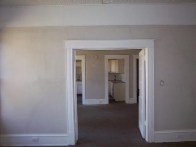 hallway with crown molding and dark colored carpet