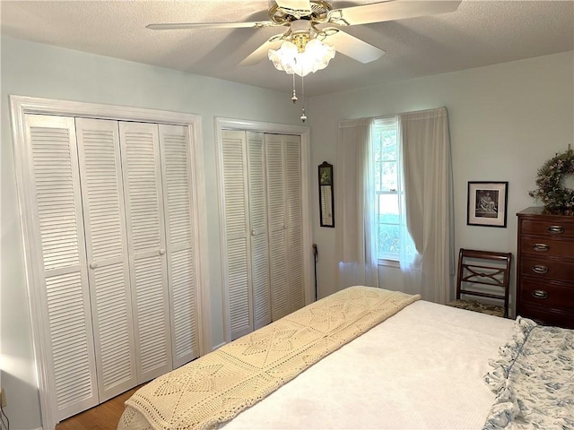 bedroom featuring wood-type flooring, a textured ceiling, two closets, and ceiling fan