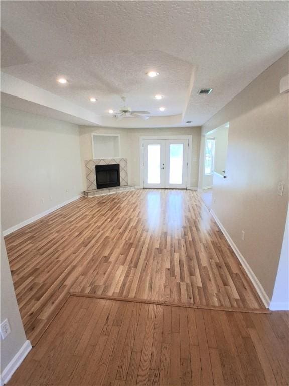 43 Shadowlake Ct, Brunswick, GA 31525 - unfurnished living room with wood finished floors, a textured ceiling, a tray ceiling, a fireplace, and french doors