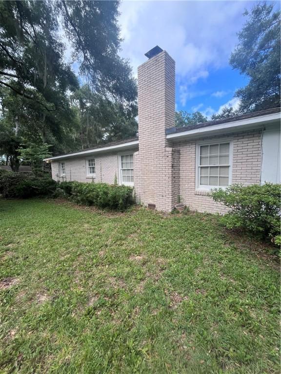 119 Saint Clair Dr, Saint Simons Island, GA 31522 - back of house featuring a chimney, brick siding, and a yard