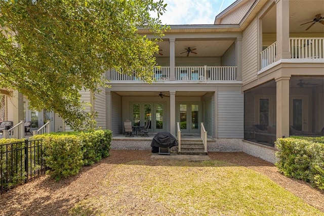 rear view of property with a ceiling fan, a balcony, fence, and french doors