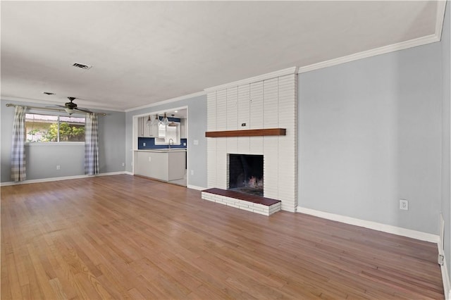 unfurnished living room featuring hardwood / wood-style floors, sink, a brick fireplace, ceiling fan, and ornamental molding