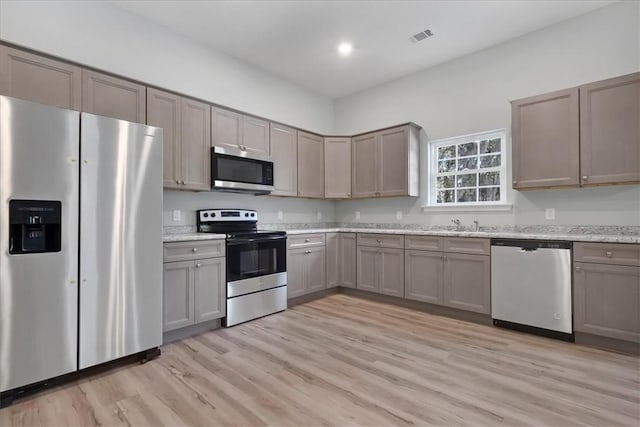 kitchen with light stone counters, light hardwood / wood-style flooring, and appliances with stainless steel finishes