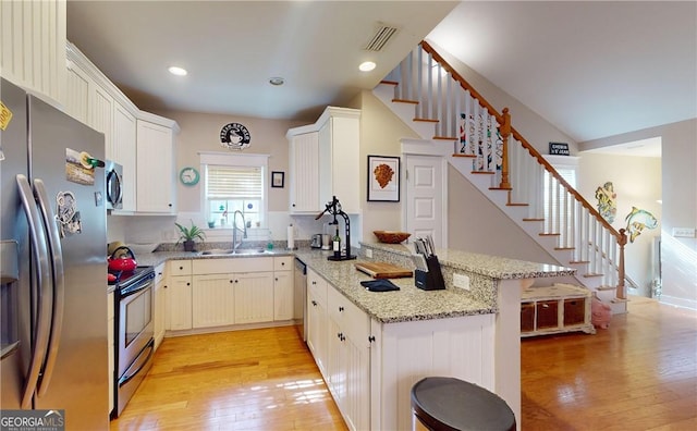 kitchen featuring sink, appliances with stainless steel finishes, light stone counters, kitchen peninsula, and a breakfast bar area