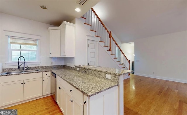 kitchen with white cabinets, sink, stainless steel dishwasher, light stone counters, and kitchen peninsula