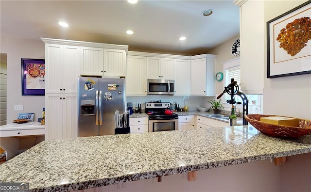 kitchen with kitchen peninsula, appliances with stainless steel finishes, white cabinetry, and light stone countertops