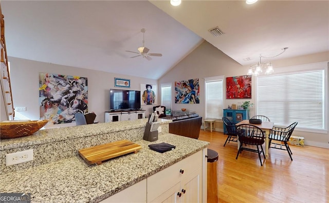 kitchen featuring ceiling fan with notable chandelier, vaulted ceiling, light hardwood / wood-style floors, and light stone counters