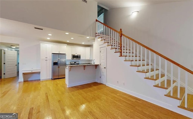 kitchen with white cabinetry, light hardwood / wood-style floors, a kitchen bar, kitchen peninsula, and stainless steel appliances