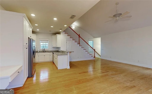 kitchen with stainless steel fridge, dark stone counters, ceiling fan, white cabinets, and light hardwood / wood-style floors