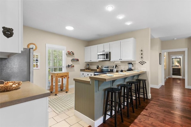 kitchen featuring baseboards, white cabinets, a breakfast bar, and stainless steel appliances
