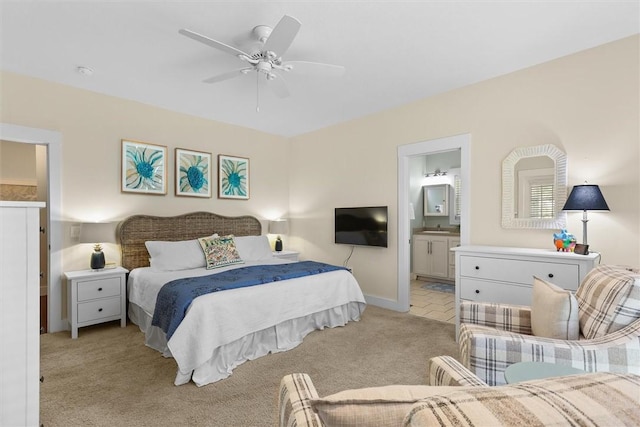 bedroom with ensuite bathroom, light carpet, baseboards, and a ceiling fan