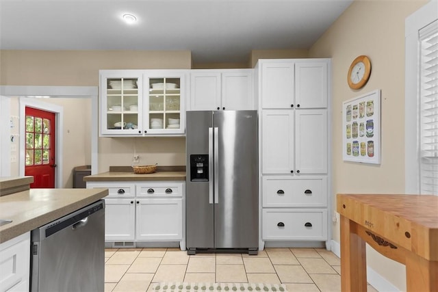 kitchen with white cabinets, appliances with stainless steel finishes, glass insert cabinets, and light tile patterned floors