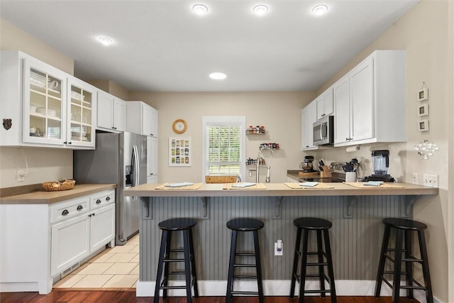 kitchen featuring a peninsula, white cabinetry, glass insert cabinets, and appliances with stainless steel finishes