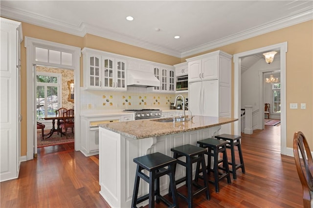 kitchen with sink, premium range hood, built in appliances, an island with sink, and white cabinets