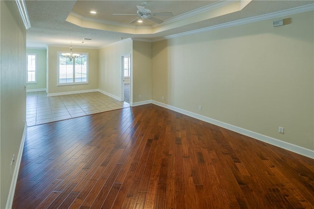 unfurnished room featuring baseboards, ornamental molding, a tray ceiling, ceiling fan with notable chandelier, and dark wood-type flooring