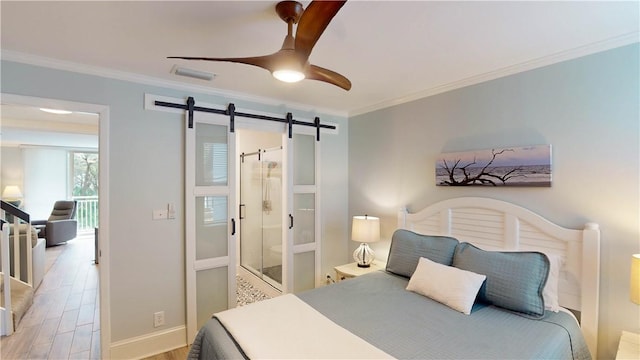 bedroom featuring visible vents, crown molding, baseboards, a barn door, and wood finished floors