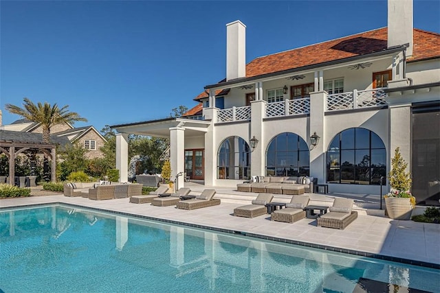 back of property with a balcony, ceiling fan, a patio area, and an outdoor living space