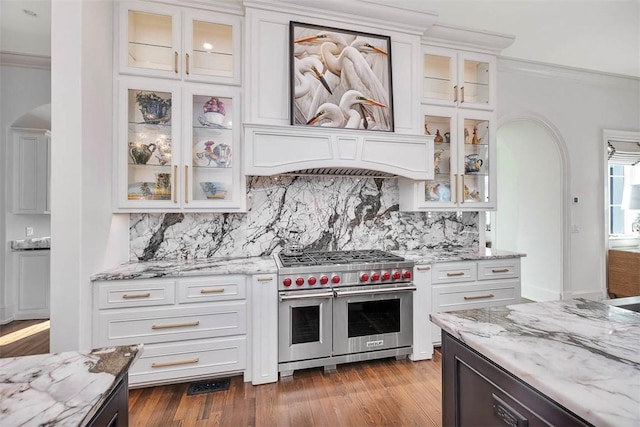 kitchen with light stone countertops, range with two ovens, ornamental molding, decorative backsplash, and white cabinets