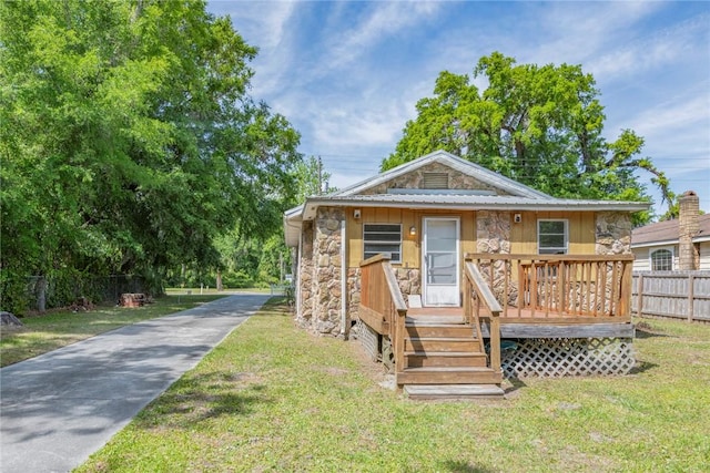 bungalow-style house with fence, a wooden deck, driveway, stone siding, and a front yard