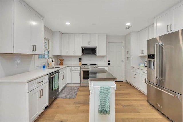 kitchen with sink, appliances with stainless steel finishes, white cabinets, a kitchen island, and light wood-type flooring