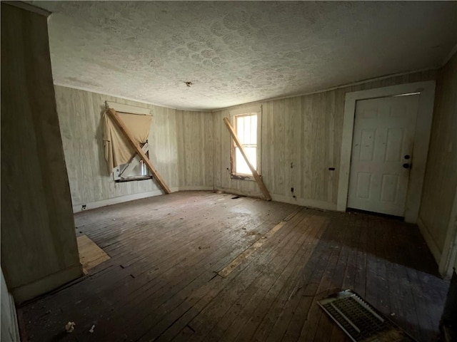 empty room featuring a textured ceiling, dark hardwood / wood-style flooring, and wooden walls