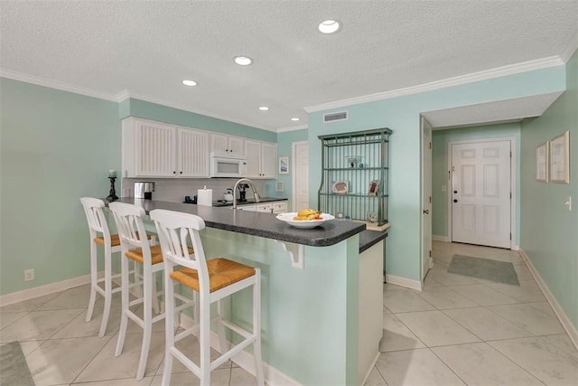 kitchen with white cabinetry, crown molding, a peninsula, and white microwave