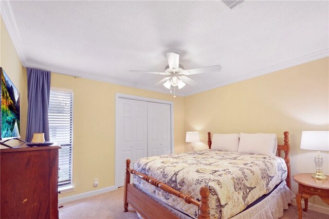 carpeted bedroom with ceiling fan, ornamental molding, and a closet