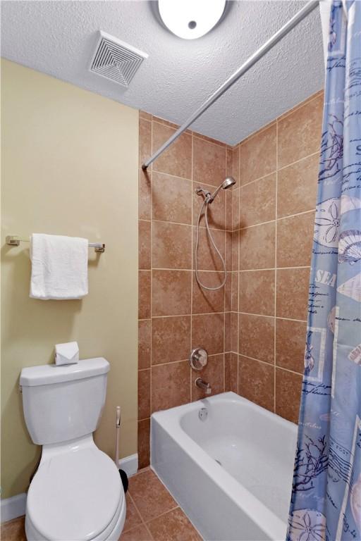 bathroom with tile patterned floors, shower / bath combo, a textured ceiling, and toilet