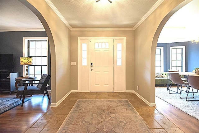 entryway featuring arched walkways, a textured ceiling, crown molding, and a wealth of natural light