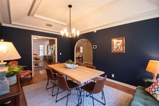 dining area featuring a tray ceiling, wood finished floors, arched walkways, an inviting chandelier, and baseboards