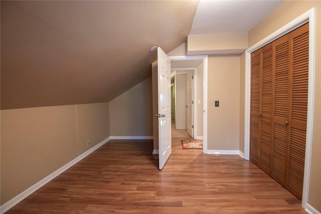 bonus room featuring vaulted ceiling, a textured ceiling, baseboards, and wood finished floors