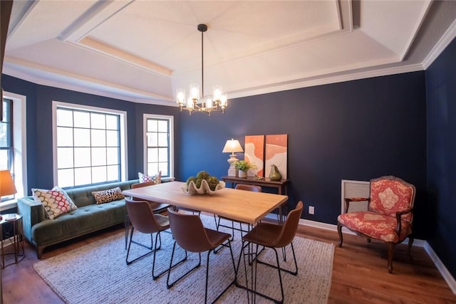 dining area with a raised ceiling, an inviting chandelier, and wood finished floors