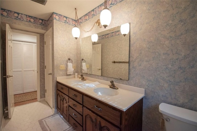 bathroom with a sink, toilet, and wallpapered walls