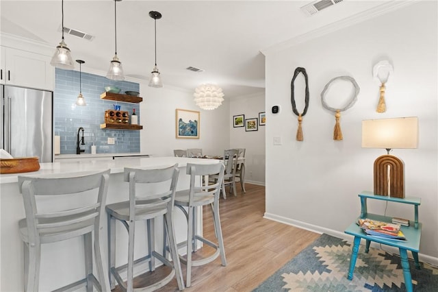 kitchen with built in fridge, light countertops, light wood-style flooring, a kitchen bar, and decorative backsplash
