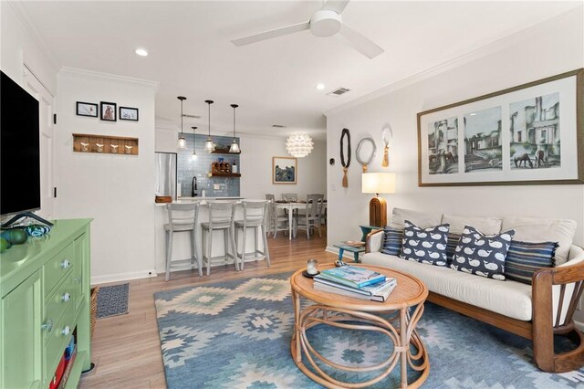living area with ornamental molding, ceiling fan, light wood finished floors, recessed lighting, and baseboards