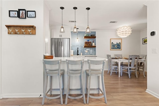 kitchen featuring high end refrigerator, decorative backsplash, light countertops, a kitchen bar, and white cabinetry
