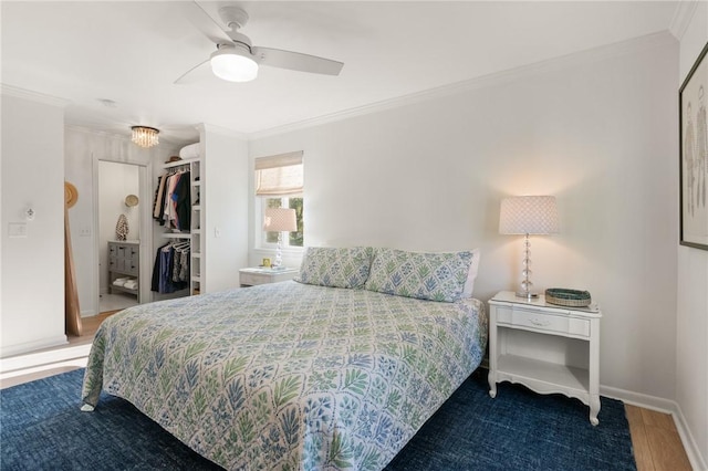 bedroom featuring ornamental molding, a ceiling fan, a closet, wood finished floors, and a walk in closet