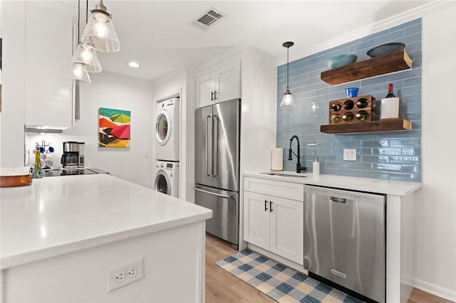 kitchen featuring appliances with stainless steel finishes, stacked washing machine and dryer, a sink, white cabinetry, and light wood-type flooring