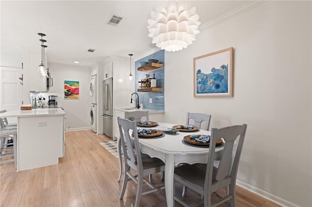 dining space featuring stacked washing machine and dryer, baseboards, light wood finished floors, a chandelier, and crown molding