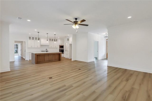 unfurnished living room featuring ceiling fan, light wood-type flooring, sink, and ornamental molding