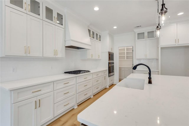 kitchen with sink, stainless steel appliances, premium range hood, decorative light fixtures, and white cabinets