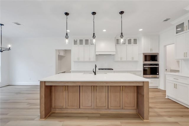 kitchen featuring white cabinets, a large island with sink, stainless steel appliances, and decorative light fixtures