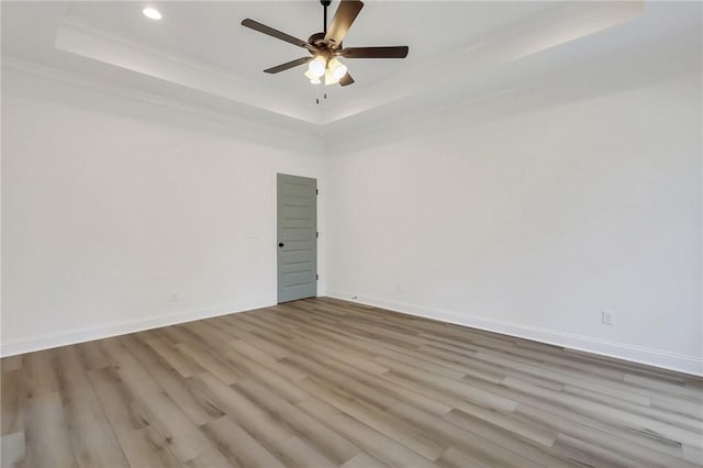 empty room featuring light hardwood / wood-style flooring, a raised ceiling, and ceiling fan