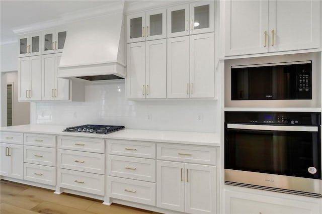 kitchen featuring white cabinets, custom exhaust hood, backsplash, and appliances with stainless steel finishes