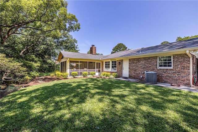 rear view of house with a lawn, a sunroom, and central AC unit