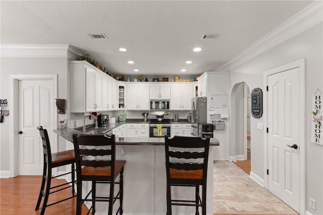 kitchen featuring stainless steel appliances, visible vents, ornamental molding, dark countertops, and arched walkways
