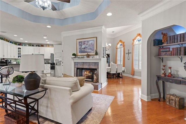 living area featuring a tiled fireplace, a ceiling fan, light wood finished floors, and baseboards