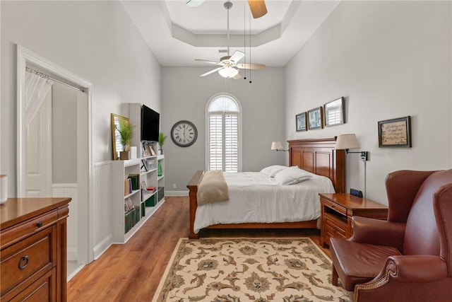 bedroom with a raised ceiling, a ceiling fan, and light wood finished floors