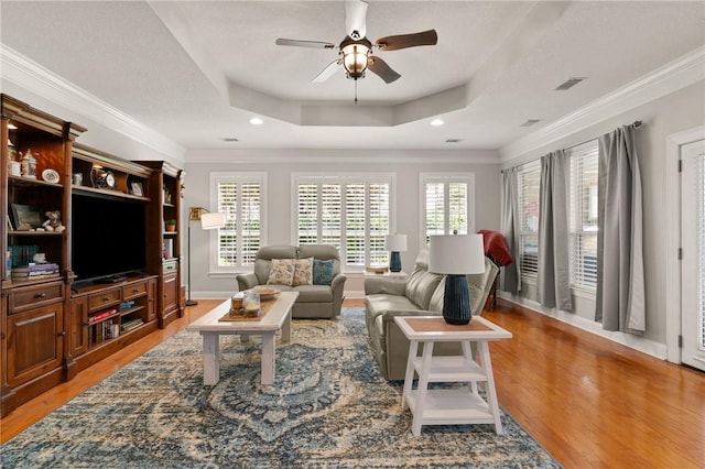 living area with visible vents, a raised ceiling, ceiling fan, and light wood-style flooring