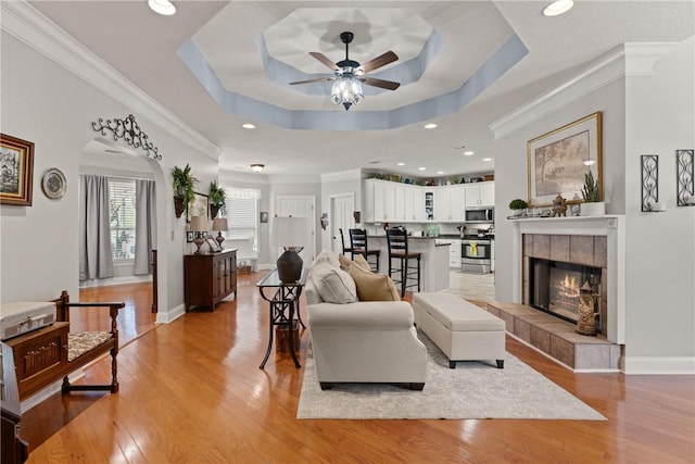 living room with ornamental molding, a ceiling fan, light wood-style floors, and a tray ceiling